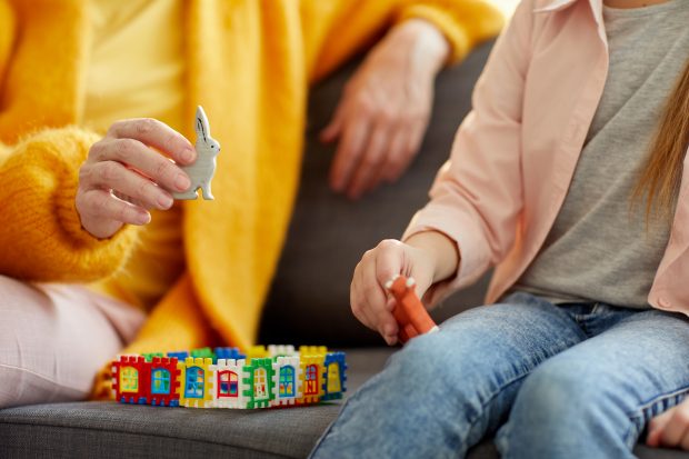 Adult sitting with child on sofa playing with toys - no faces shown