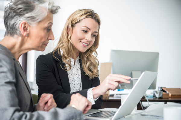 two women sitting by a laptop at a desk