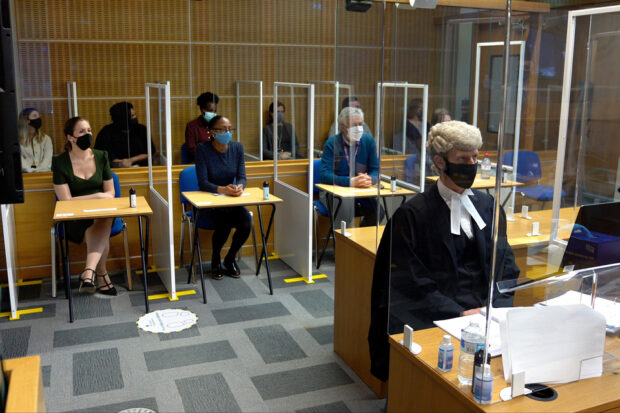 Photo of a mock trial with the barrister and jury members behind screens and wearing facemasks