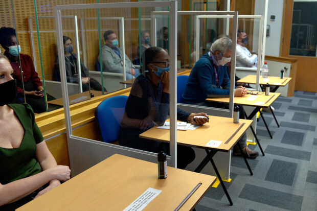 Members of the jury in a mock trial sitting between plexiglass screens and wearing masks