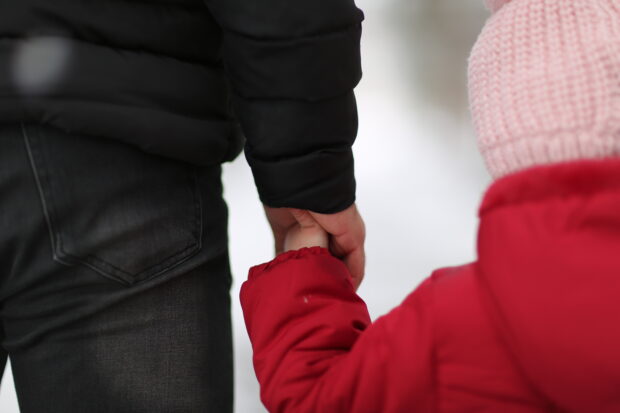 Close up photo of child walking and holding an adult's hand (faces not seen)