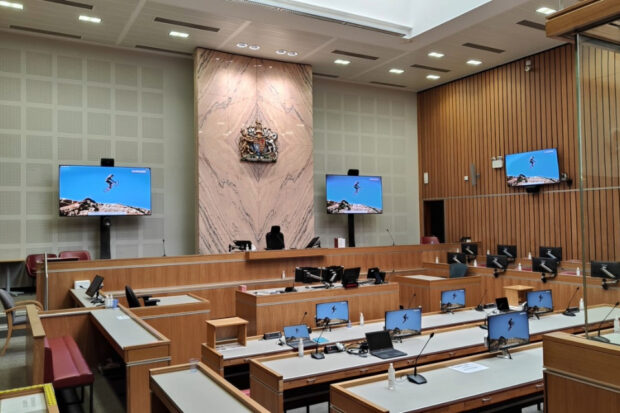 Empty courtroom with wooden benches, desks and multiple screens.